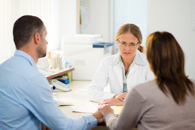 Couple sits at a table having a conversation with a medical provider.