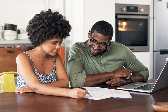 couple sits at table looking at papers on the table together.