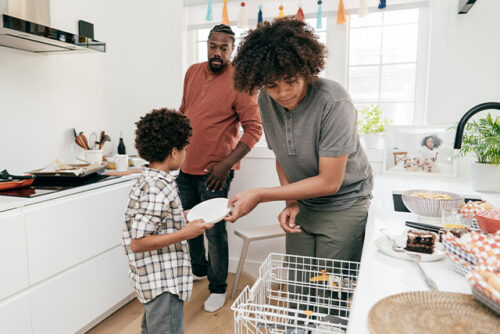 Family stands in the kitchen removing dishes from the dishwasher