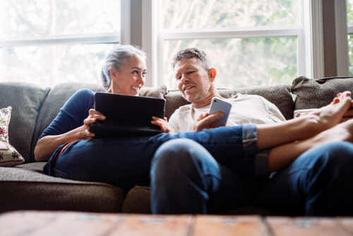 A couple sits on the couch smiling at each other.