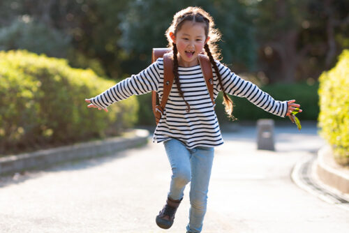 6 year old girl runs with backpack on while smiling
