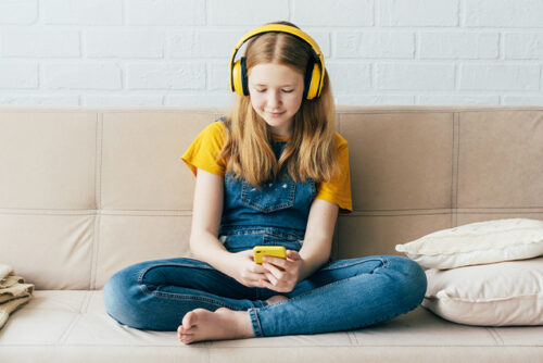 Girl sits on the couch with headphones on looking at a smart phone