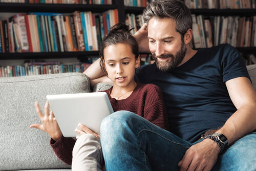 Daughter and father sit on couch looking at ipad