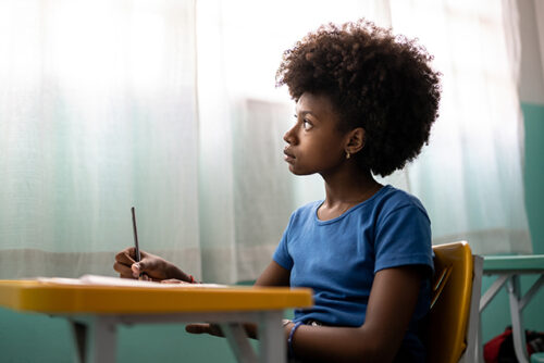 Child sits at desk with a pencil in hand looking out the window