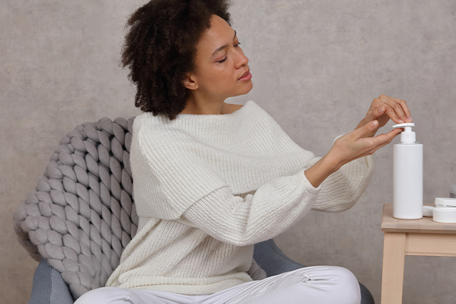 woman sitting down and applying skin care product