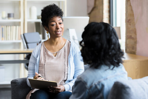Two women sit on a couch talking.