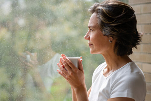 Woman sips from a mug while looking out the window.