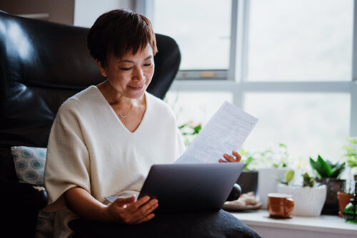Seated woman looks at computer screen while holding a piece of paper.