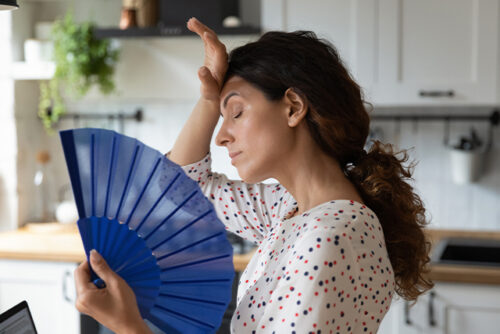 Woman holds fan while holding her hand over her head.