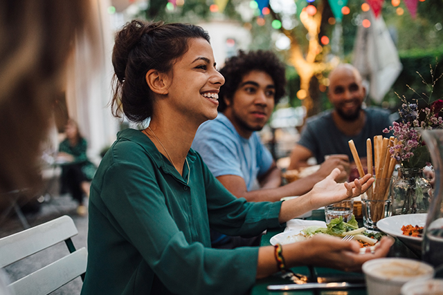 a woman sits at a dining table surrounded by people and food