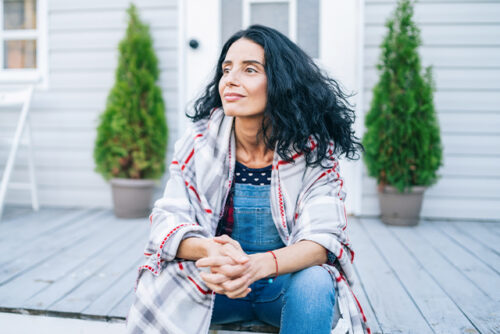 Woman sits on porch with hands clasped, looking off camera
