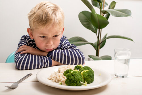 Child sits at the table with arms crossed staring at his plate.