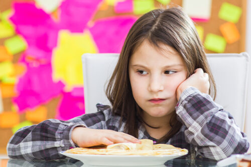 Child sits at the table looking upset at her plate.