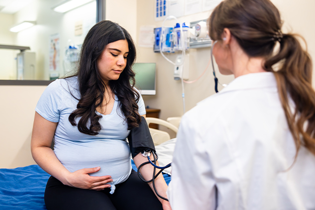 a pregnant woman sitting in a doctor's office speaks with a female physician