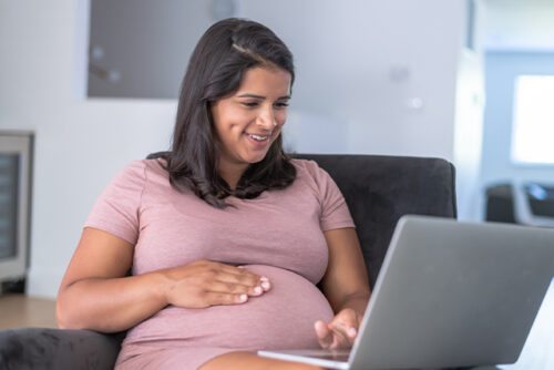 Pregnant woman looks at computer smiling while holding her bump.