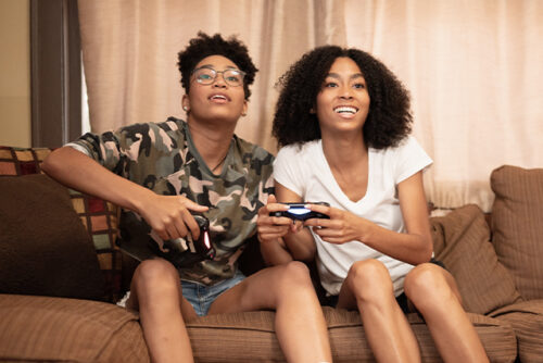 Two teenagers sit on a couch looking over the camera and smiling