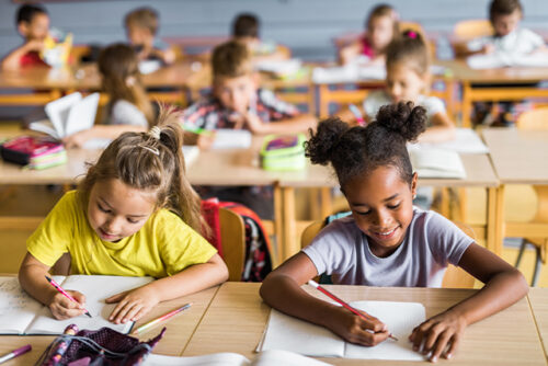 Young students in a classroom sit at their desks working on paper