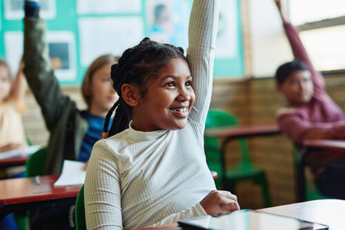 A girl raises her hand in a classroom and smiles