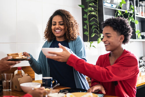 Family sits at a table sharing a meal and smiling