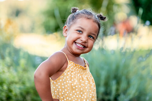 Little girl smiles while standing in the grass, her hand on her hip