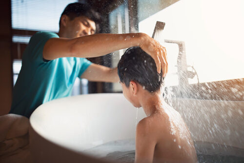 Child sits in tub and parent washes their hair