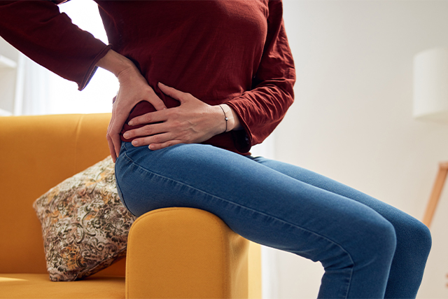woman holds hip while sitting on sofa arm