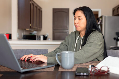 a woman sits at her laptop typing on the keyboard