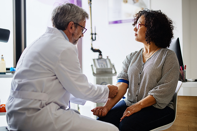 a woman sits in a doctor's office with a tourniquet on her arm, waiting to have her blood drawn