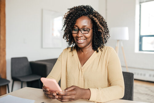 Woman sitting at desk smiles at her phone