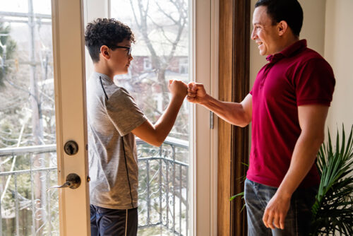 Man and boy fist bump through a doorway.