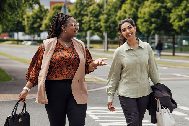 two women walk alongside one another. one woman is talking and the other is listening