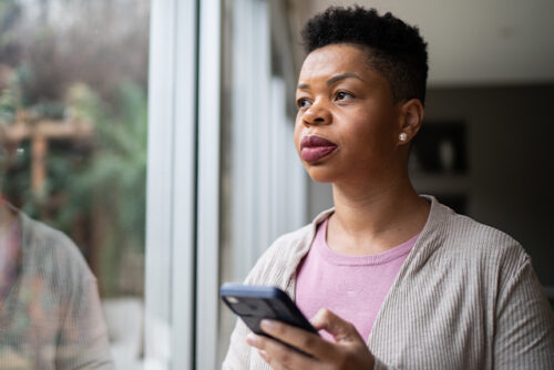 Woman holds phone in one hand while looking out the window.