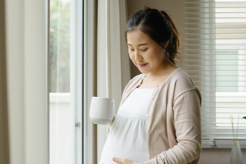 Pregnant woman holds mug in one hand