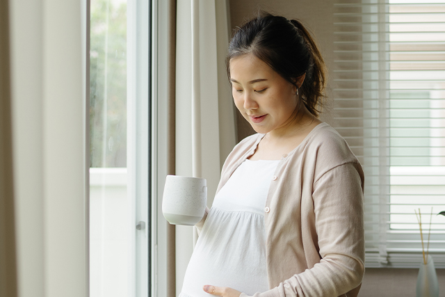 Pregnant woman holds mug in one hand