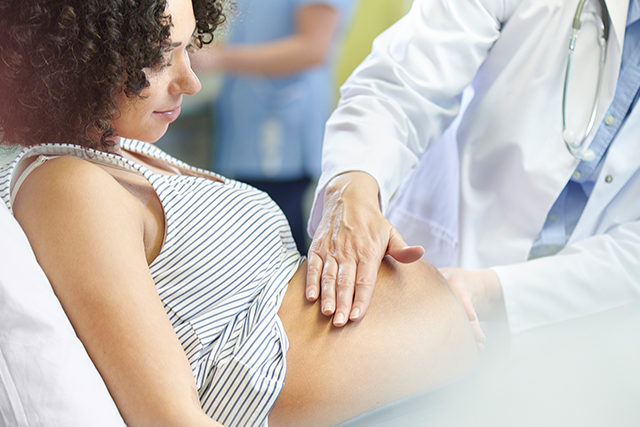 Pregnant woman has her stomach felt by a provider
