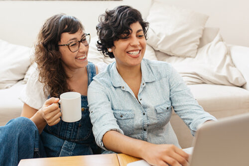 Two women look at a computer screen and smile