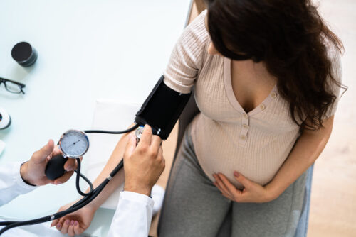 Close-up Of Male Doctor Measuring Blood Pressure Of Pregnant Woman In Clinic