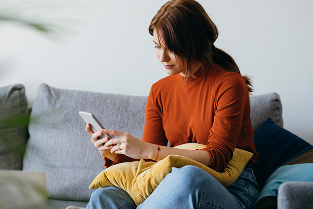 Woman, seated on couch, looks at her phone