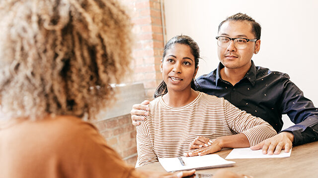 two people sit at a table, facing a third person