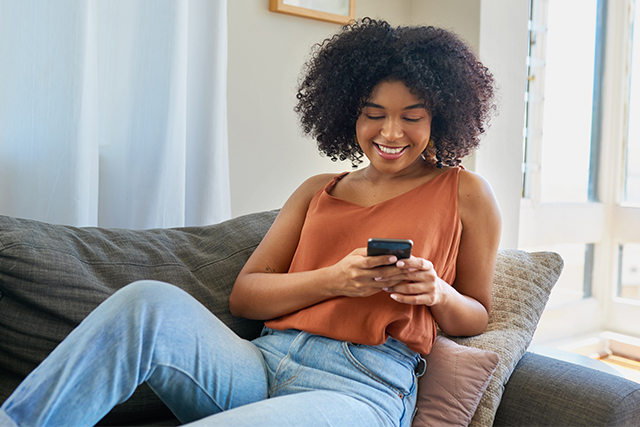 woman sits on couch, smiling at her phone
