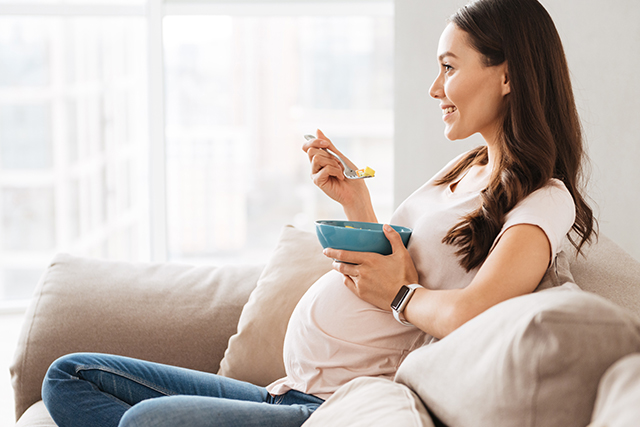 Woman sitting on couch eats from a bowl.