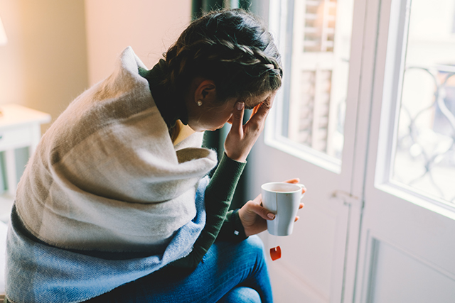 Woman wrapped in blanket holds her head