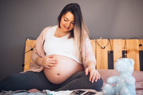 Pregnant woman sits on the bed holding her stomach
