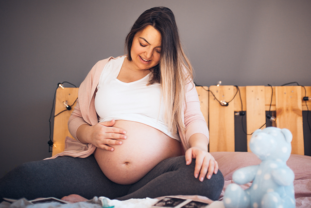Pregnant woman sits on the bed holding her stomach