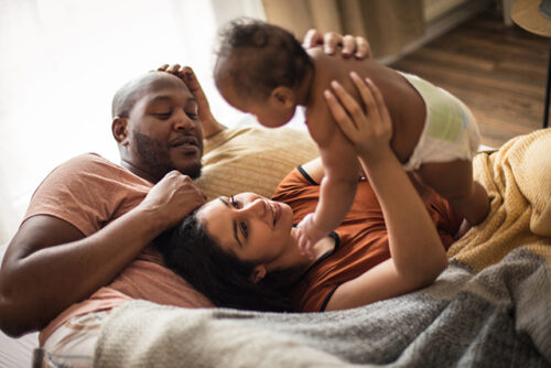couple reclines, women lifts baby over her head, man looks at her