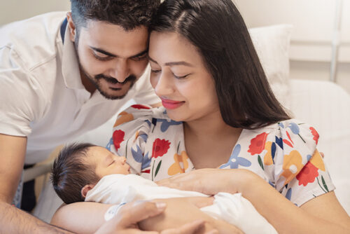 A woman and man lean over their baby and smile