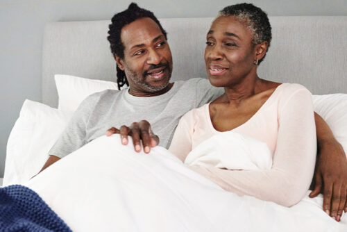 Couple sits up in bed; man looks at woman
