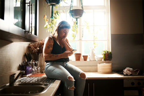 Woman, seated on kitchen counter, looks at her phone