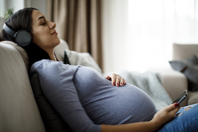 Pregnant woman with eyes closed reclines with headphones on