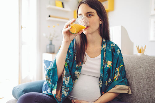A pregnant woman drinks a cup of orange juice